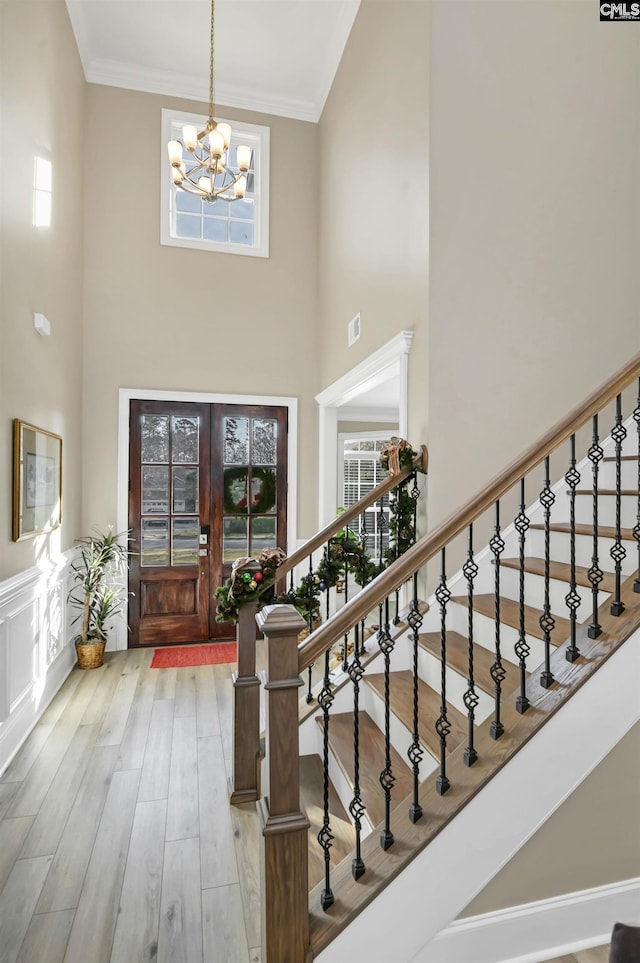 entryway with french doors, a high ceiling, crown molding, an inviting chandelier, and hardwood / wood-style floors