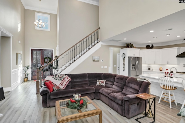 living room featuring a notable chandelier, light hardwood / wood-style floors, ornamental molding, and french doors