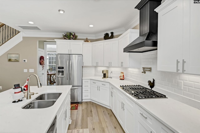 kitchen featuring white cabinetry, sink, stainless steel appliances, wall chimney range hood, and crown molding