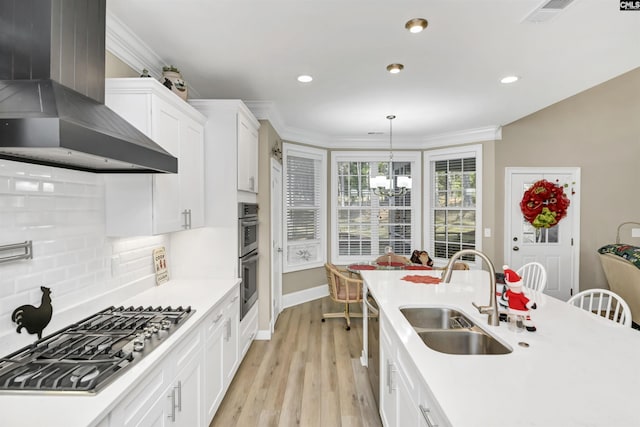 kitchen with sink, hanging light fixtures, wall chimney range hood, white cabinets, and appliances with stainless steel finishes