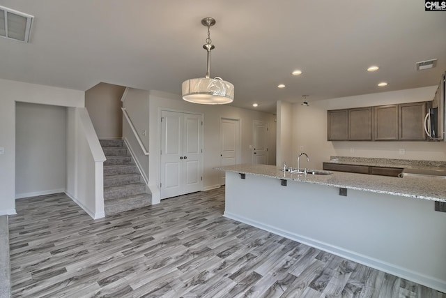 kitchen featuring a kitchen bar, light stone countertops, sink, pendant lighting, and light hardwood / wood-style flooring