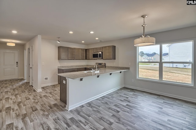 kitchen with kitchen peninsula, sink, decorative light fixtures, light hardwood / wood-style flooring, and a breakfast bar area