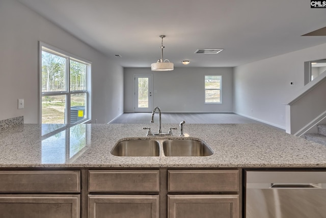 kitchen with plenty of natural light, light stone counters, sink, and decorative light fixtures