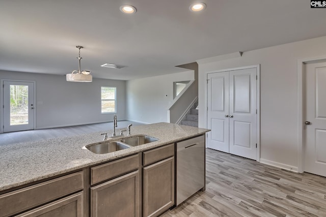 kitchen featuring dishwasher, sink, light stone countertops, light wood-type flooring, and decorative light fixtures