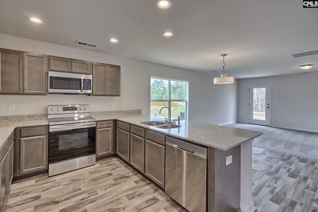 kitchen featuring sink, light hardwood / wood-style flooring, kitchen peninsula, pendant lighting, and appliances with stainless steel finishes