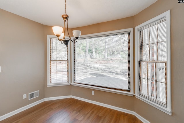 unfurnished dining area with hardwood / wood-style floors, an inviting chandelier, and a healthy amount of sunlight