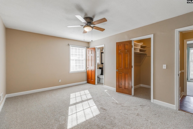 unfurnished bedroom featuring ensuite bathroom, a walk in closet, ceiling fan, light colored carpet, and a closet