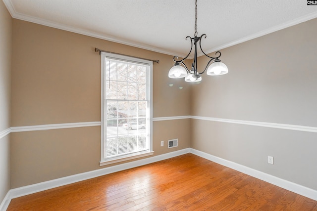 unfurnished dining area with a chandelier, a textured ceiling, hardwood / wood-style flooring, and crown molding