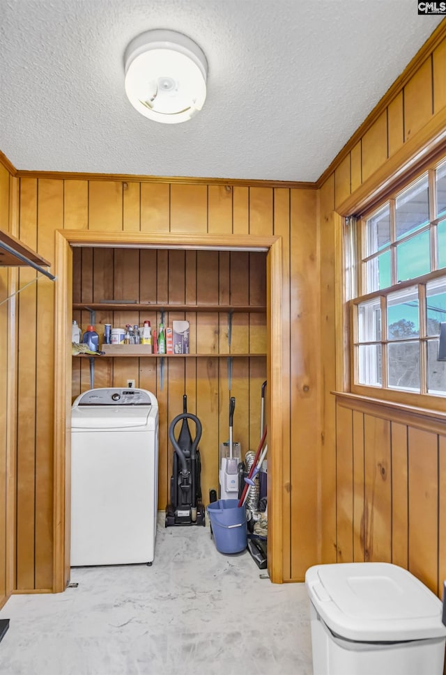 clothes washing area featuring a textured ceiling, washer / clothes dryer, and wooden walls