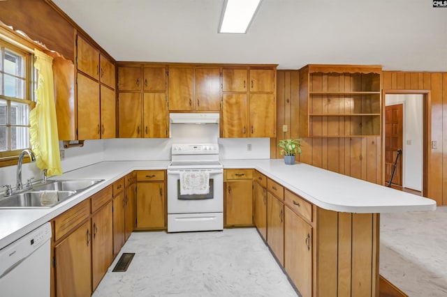 kitchen with kitchen peninsula, wood walls, sink, and white appliances