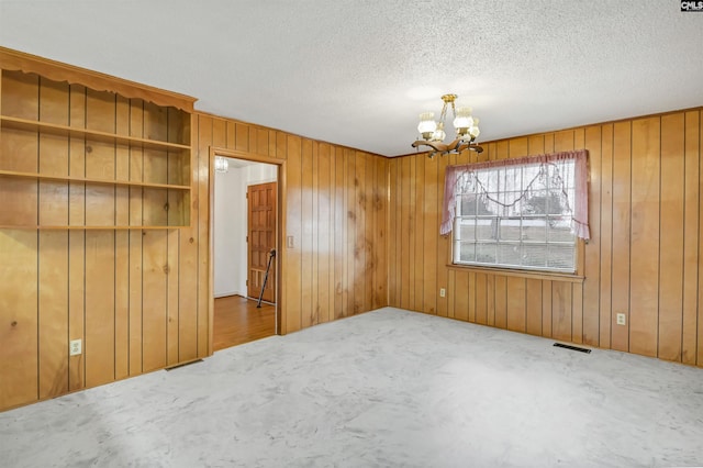 carpeted spare room featuring a textured ceiling, wooden walls, and a notable chandelier