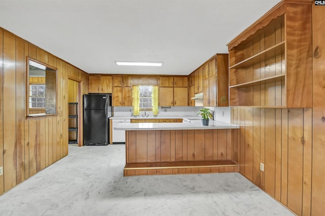 kitchen featuring dishwasher, wood walls, stove, black refrigerator, and kitchen peninsula