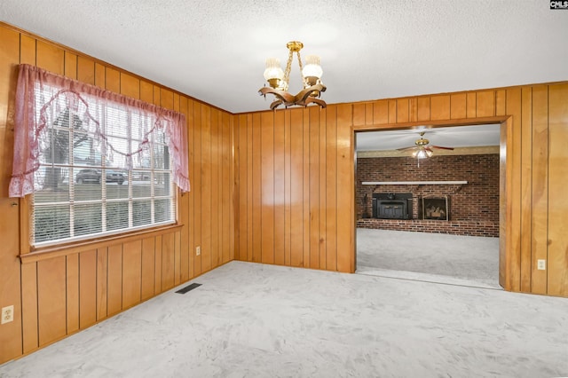 spare room featuring carpet, ceiling fan with notable chandelier, wooden walls, a fireplace, and a textured ceiling