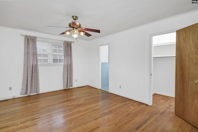 unfurnished bedroom with ceiling fan, light hardwood / wood-style flooring, a textured ceiling, a walk in closet, and a closet