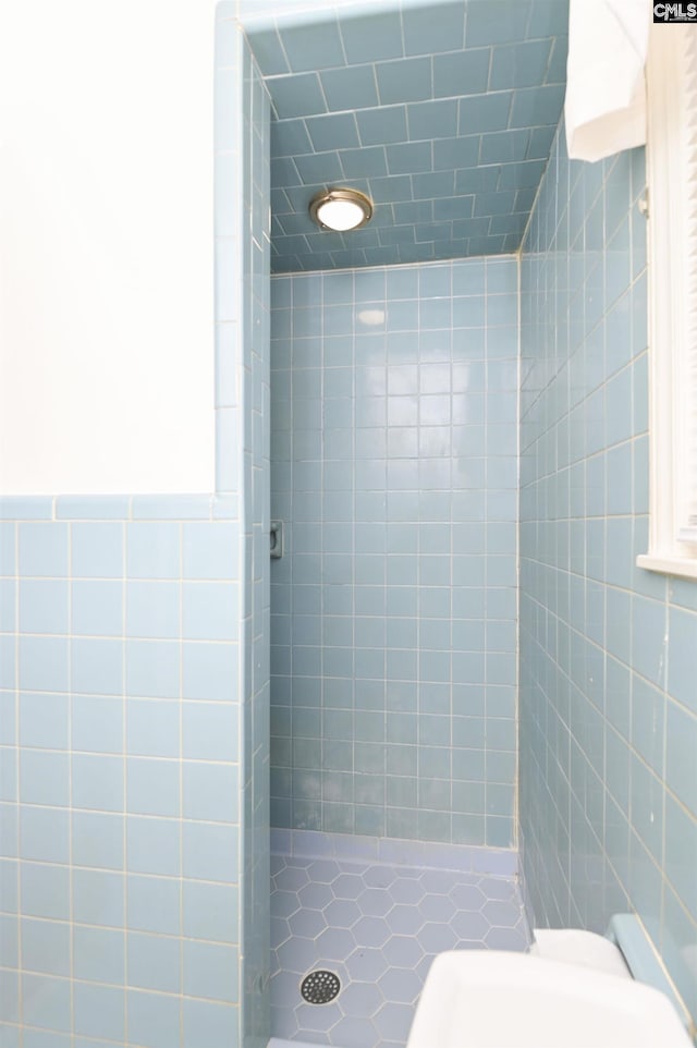 bathroom with tiled shower, toilet, and tile walls