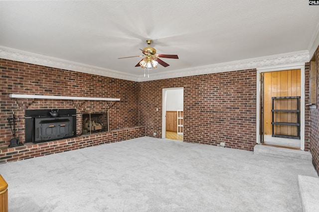 unfurnished living room with carpet flooring, ceiling fan, crown molding, and brick wall