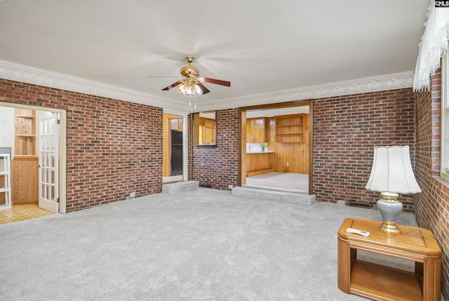 unfurnished living room with ceiling fan, crown molding, brick wall, and light carpet