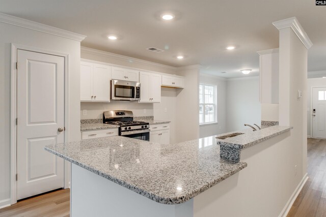 kitchen with kitchen peninsula, light stone countertops, light wood-type flooring, appliances with stainless steel finishes, and white cabinetry