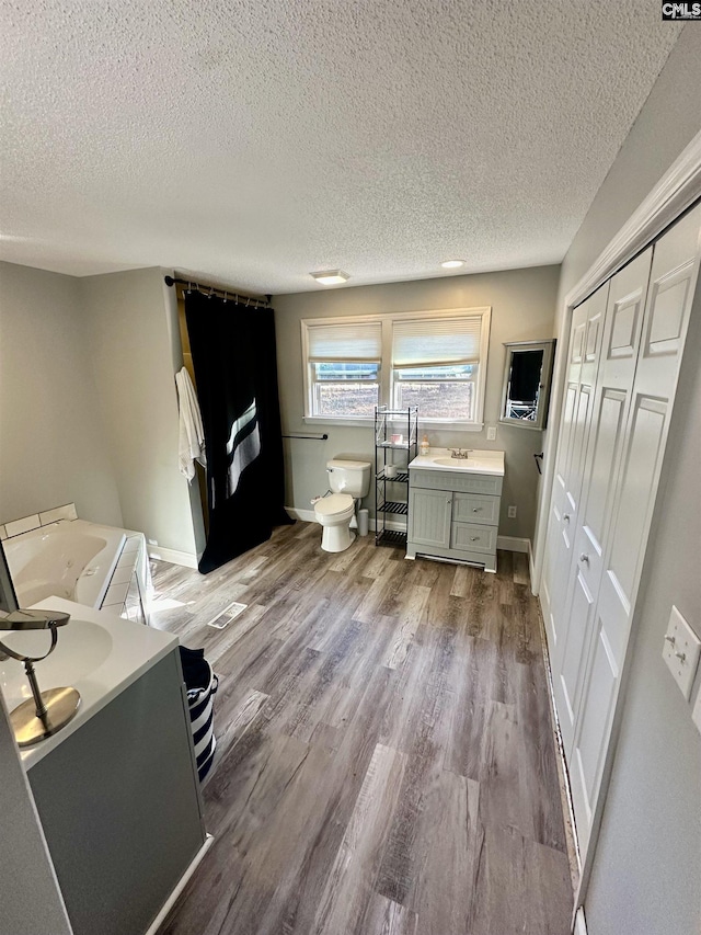 bathroom with hardwood / wood-style flooring, vanity, a bath, a textured ceiling, and toilet