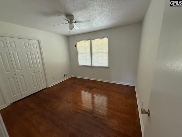 unfurnished bedroom with a textured ceiling, baseboards, visible vents, dark wood-style floors, and a closet