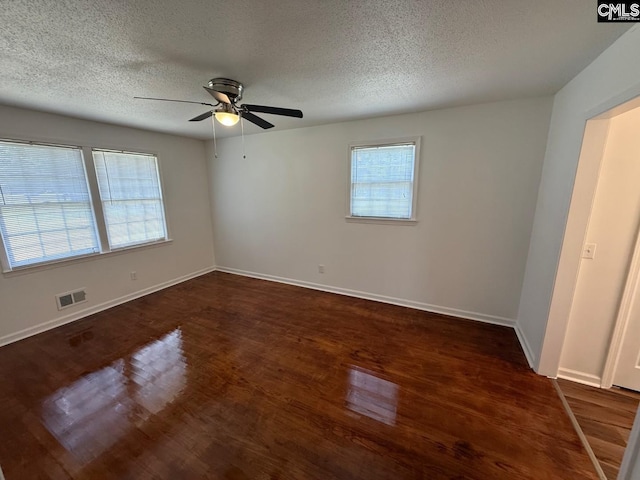unfurnished room featuring visible vents, dark wood-style flooring, baseboards, a textured ceiling, and a ceiling fan