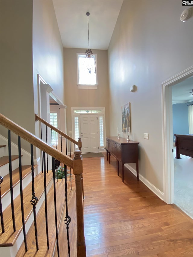 entryway with hardwood / wood-style floors, a towering ceiling, and a notable chandelier