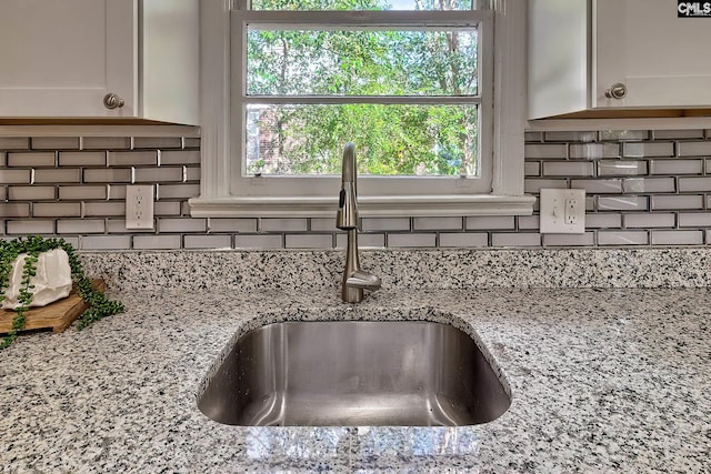 interior details featuring decorative backsplash, white cabinetry, light stone countertops, and sink