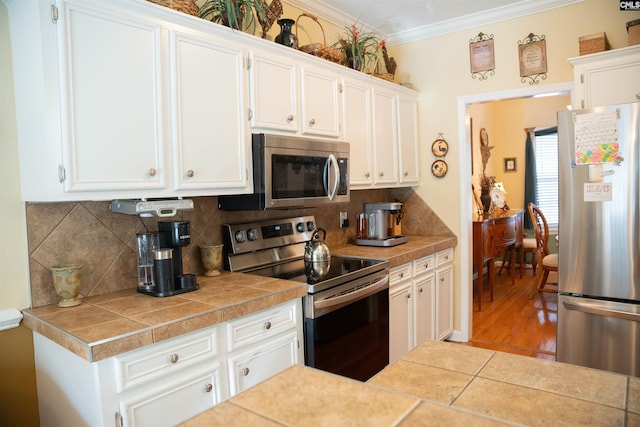 kitchen featuring backsplash, tile counters, white cabinets, and stainless steel appliances