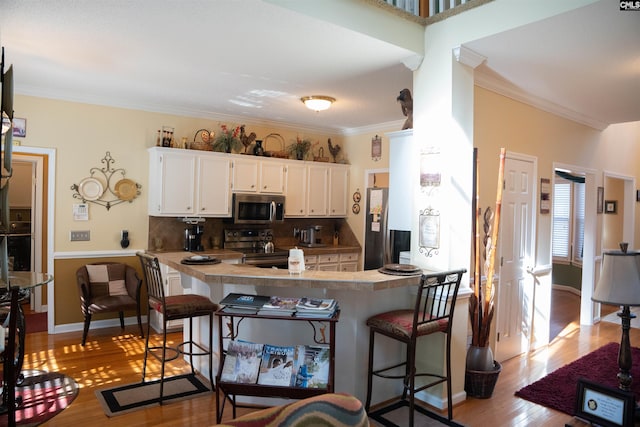 kitchen featuring white cabinets, a kitchen breakfast bar, decorative backsplash, appliances with stainless steel finishes, and kitchen peninsula