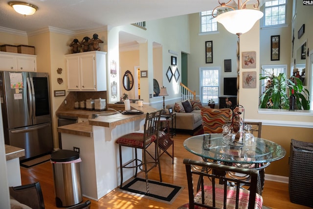 kitchen featuring stainless steel refrigerator, white cabinetry, hanging light fixtures, tasteful backsplash, and a kitchen breakfast bar