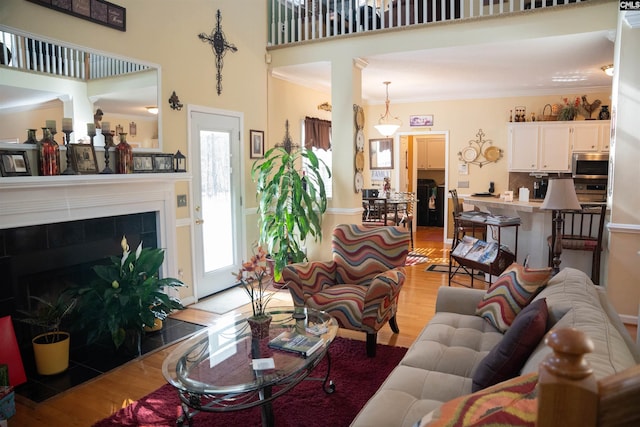 living room with light hardwood / wood-style floors, ornamental molding, a high ceiling, and a tiled fireplace