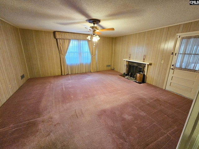 unfurnished living room with ceiling fan, wood walls, carpet, and a textured ceiling