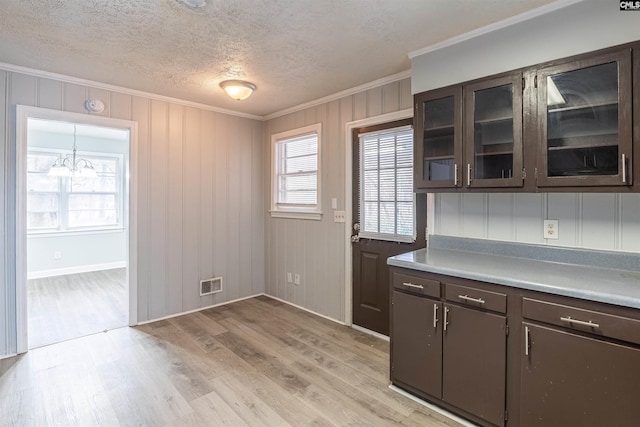 kitchen featuring pendant lighting, crown molding, light hardwood / wood-style flooring, dark brown cabinets, and a chandelier