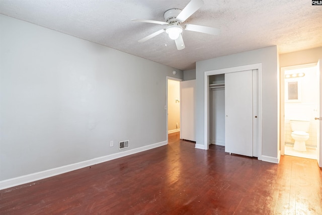 unfurnished bedroom featuring ensuite bath, a textured ceiling, ceiling fan, dark hardwood / wood-style floors, and a closet