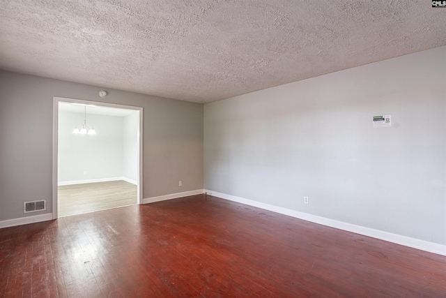 unfurnished room with a textured ceiling, dark wood-type flooring, and a chandelier