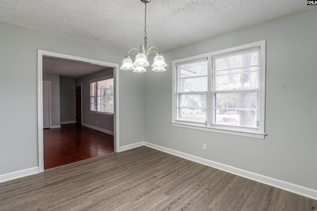 unfurnished dining area with dark wood-type flooring, a textured ceiling, and an inviting chandelier