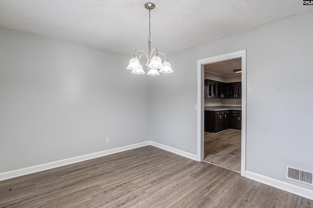 spare room featuring hardwood / wood-style floors, a notable chandelier, and a textured ceiling