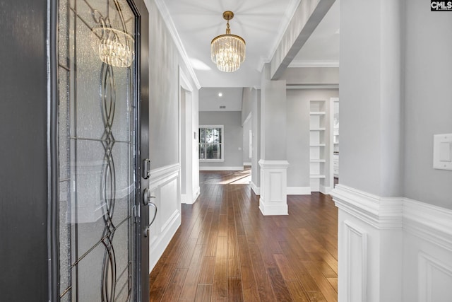 foyer entrance featuring ornate columns, dark wood-type flooring, ornamental molding, and a notable chandelier