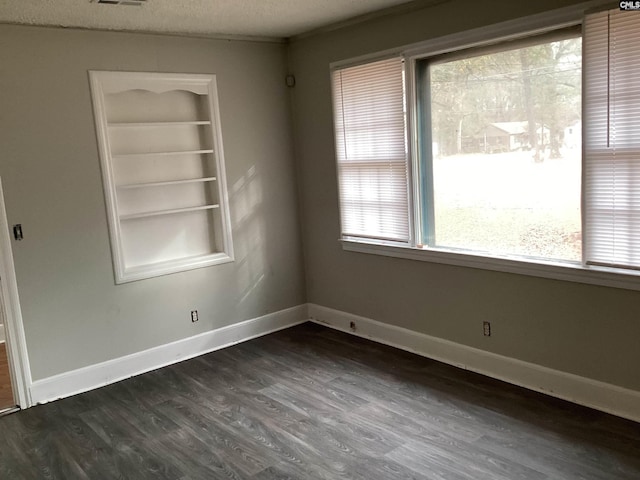 empty room featuring built in shelves, a wealth of natural light, dark wood-type flooring, and a textured ceiling