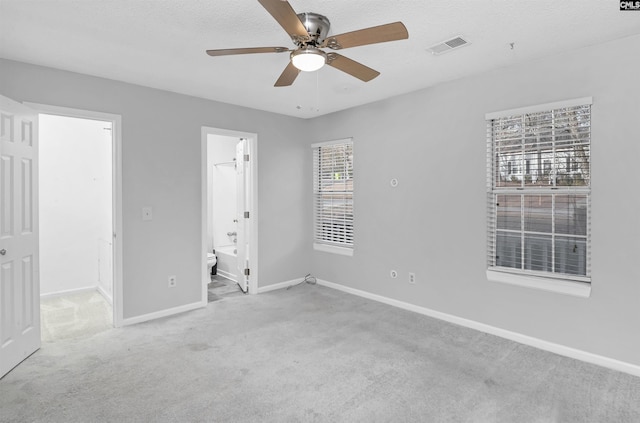 unfurnished bedroom featuring ensuite bath, ceiling fan, light colored carpet, and a spacious closet