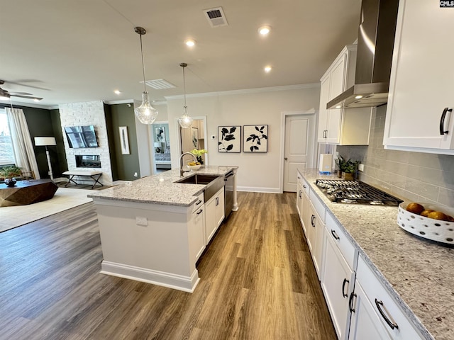 kitchen with a center island with sink, white cabinets, wall chimney exhaust hood, a fireplace, and a sink