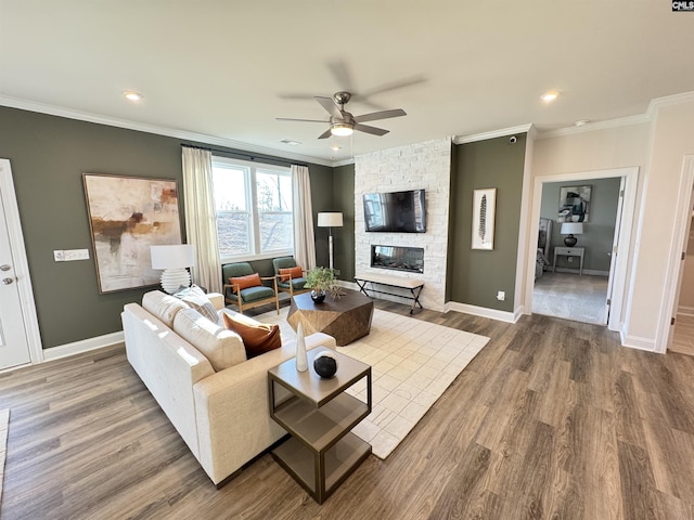 living area featuring crown molding, baseboards, wood finished floors, and a stone fireplace