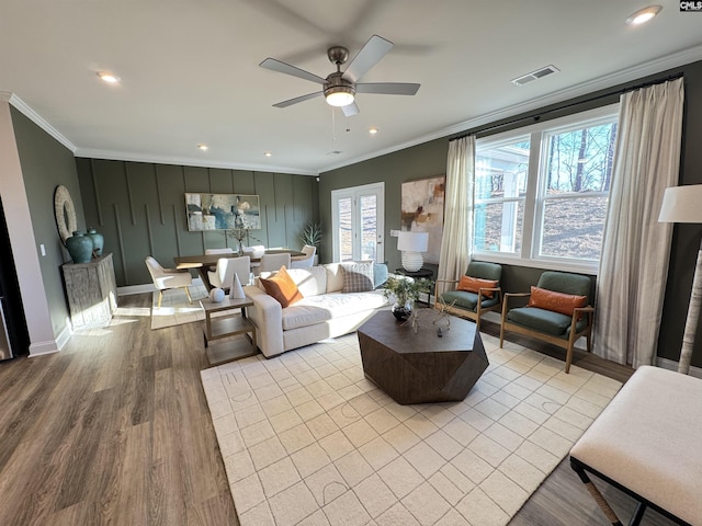 living room with visible vents, ornamental molding, ceiling fan, light wood-type flooring, and baseboards