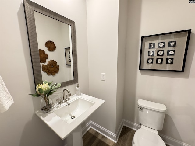 half bath featuring toilet, a sink, baseboards, and wood finished floors