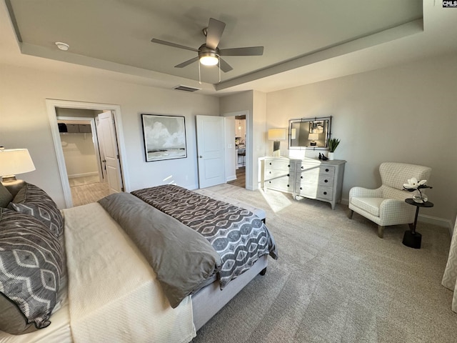 bedroom with ceiling fan, light colored carpet, visible vents, baseboards, and a raised ceiling