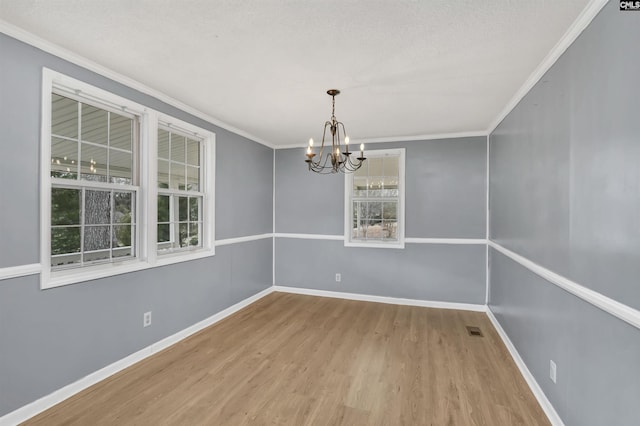 empty room with hardwood / wood-style floors, a chandelier, plenty of natural light, and ornamental molding