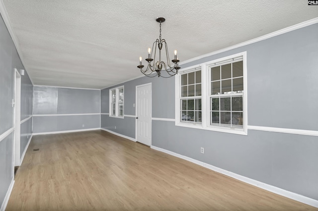 spare room with hardwood / wood-style floors, ornamental molding, a textured ceiling, and an inviting chandelier