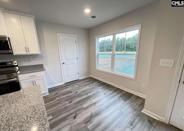 kitchen featuring hardwood / wood-style floors, appliances with stainless steel finishes, white cabinetry, and light stone counters