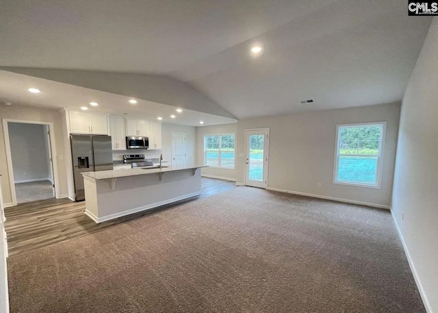 kitchen with light carpet, a center island with sink, appliances with stainless steel finishes, white cabinets, and a breakfast bar