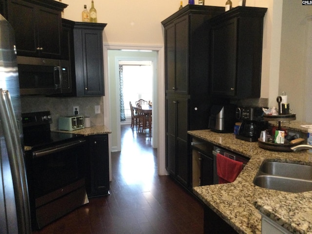 kitchen with appliances with stainless steel finishes, sink, backsplash, light stone counters, and dark wood-type flooring